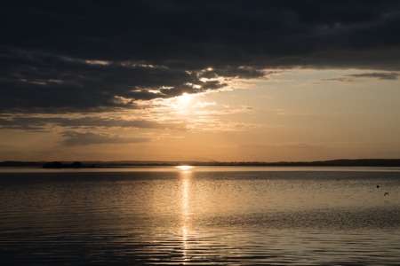 sunset over the water is hidden behind cloudsの写真素材