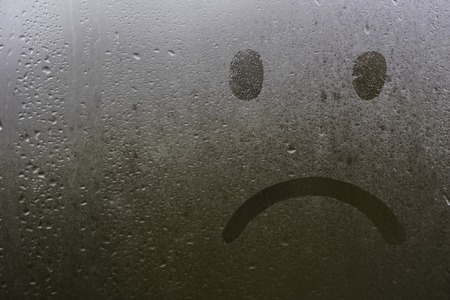 sad face on a wet window glass in the autumn.の写真素材