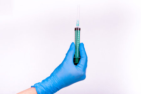 Hand in blue glove holding syringe on white background.の写真素材