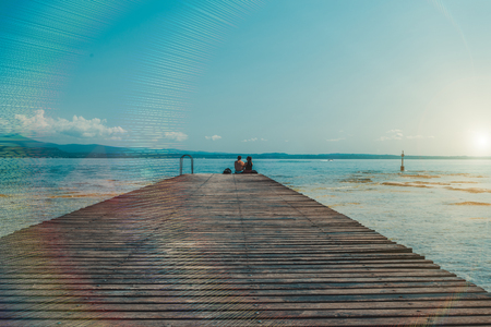 The couple sitting on the pier dangling legs observed sunset over the lake.の写真素材