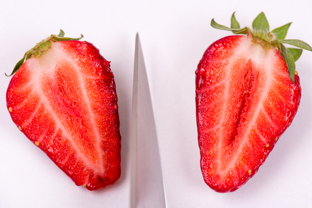 cutting strawberries on a white background with a metal chefs knifeの写真素材