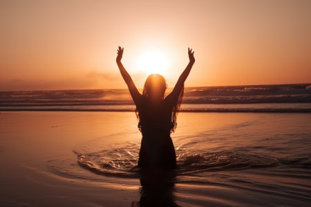 Silhouette of happy woman with raised hands on the beach at sunset. Generative AI.の素材