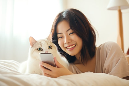 Beautiful Asian woman using mobile phone on bed at homeの素材
