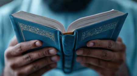A man is reading a book with his hands. The book is blue and has gold trim. The man is wearing a blue shirtの素材