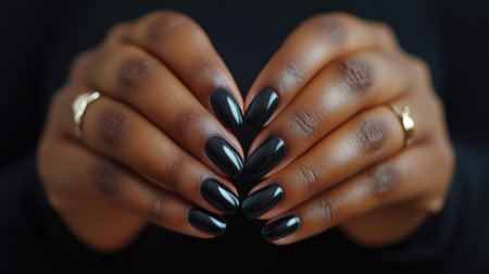 A woman's hands are shown with long, black fingernails. The nails are painted black and appear to be well-maintained. The woman's hands are clasped togetherの素材