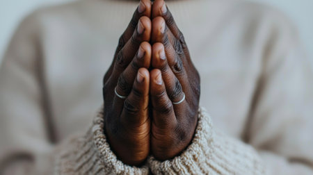 Two hands are gently pressed together in a gesture of mindfulness. The focus is on the textured skin, rings on the fingers, and warm, cozy sweater fabric surrounds them.の素材