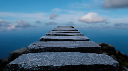 A long stone pathway stretches over calm water, inviting exploration. Fluffy clouds drift in an expansive blue sky, creating a peaceful atmosphere in nature.の素材