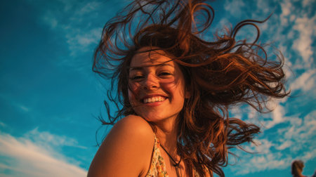A woman smiles brightly as her hair dances in the wind capturing the essence of a beautiful beach day.の素材