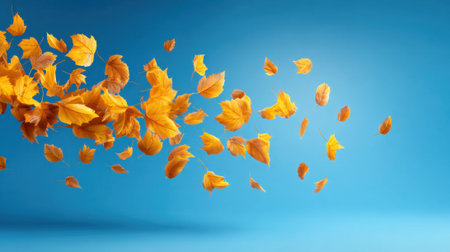 Golden leaves float gracefully in the air, creating a vibrant display against a clear blue sky. This scene captures the beauty of autumn outdoors on a sunny day.の素材