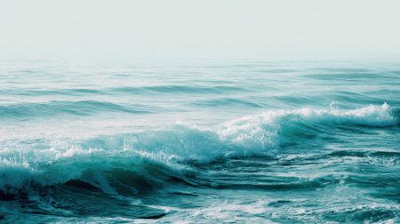 Soft waves are rolling in at a tranquil beach during a peaceful morning. The water shimmers in various shades of blue under the clear sky, creating a calming atmosphere.の素材