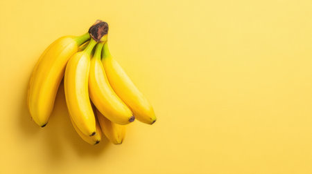 A cluster of ripe yellow bananas rests on a vibrant yellow background, highlighting their fresh appearance. Perfect for a nutritious snack or smoothie ingredient.の素材