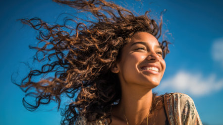 A happy woman with curly hair smiles broadly as the wind plays with her hair at the beach.の素材