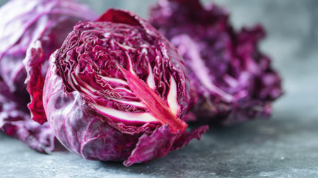 A vibrant red cabbage sits on a gray surface cut in half to display its intricate layers and deep purple hues. The fresh vegetable highlights its crisp texture and natural beauty.の素材
