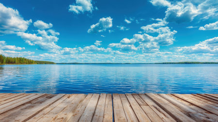 A serene lake scene features a wooden dock extending over calm waters. Fluffy white clouds drift across a bright blue sky, reflecting the tranquility of nature. Perfect for relaxation.の素材