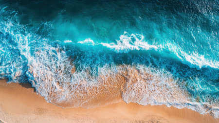 Vibrant blue waves roll onto a sandy beach, creating a rhythmic pattern as they crash. The sunlight reflects off the water, enhancing the serene atmosphere on this beautiful coastline.の素材