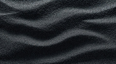 The texture of black sand displays gentle waves and ripples, illuminated by sunlight on a sunny day at the beach, showing unique natural beauty.の素材