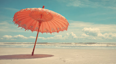 A bright pink parasol leans gracefully on the sandy beach, casting a small shadow. Gentle waves lap at the shore under a clear blue sky scattered with clouds.の素材