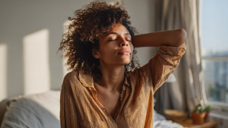A woman sits in a serene bedroom, eyes closed and face relaxed. She wears a striped shirt and enjoys the gentle sunlight streaming through the window, creating a peaceful atmosphere.の素材