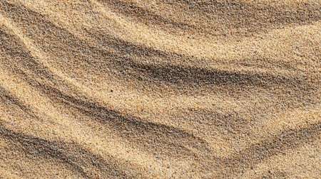 The close-up view showcases fine grains of sand with gentle ripples, reflecting soft light in a serene beach setting during the late afternoon, creating a calming atmosphere.の素材