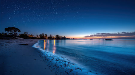 A peaceful beach at dusk showcases gentle waves lapping at the shore. Stars twinkle above, while the last light of sunset casts vibrant reflections on the water's surface.の素材
