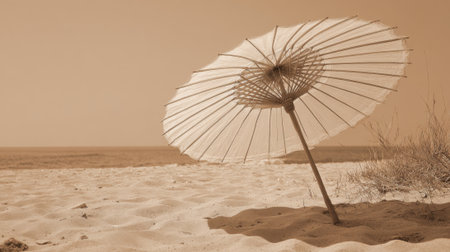 A vintage-styled parasol stands alone on a sandy beach under a clear sky. Soft waves roll in the background, creating a calm and peaceful atmosphere.の素材