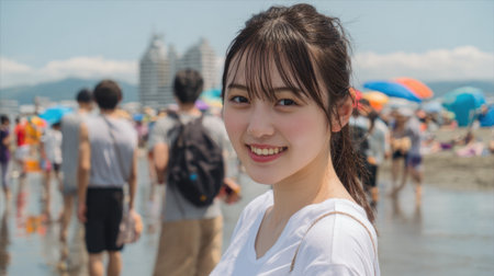 A young woman smiles warmly at the camera while enjoying a sunny day at the beach. Crowds gather behind her, with colorful umbrellas dotting the sandy shore.の素材