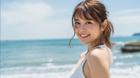 A woman is smiling joyfully while standing near the water's edge on a sunny beach day. The bright sunlight enhances her cheerful expression and the beautiful scenery around her.の素材
