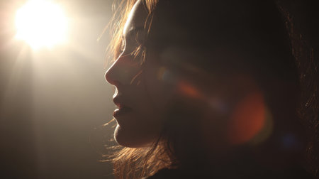 A woman in profile stands quietly her features lit in a warm glow evoking peace.の素材