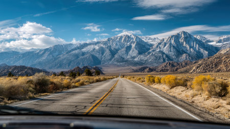 A scenic road stretches towards snow capped mountains under a vibrant blue sky framed by autumn foliage.の素材