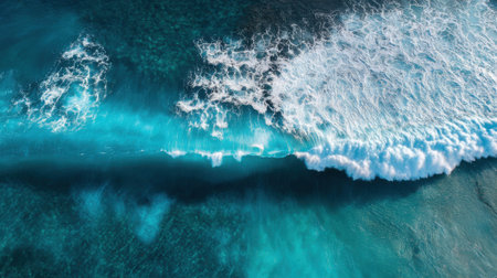 Bright turquoise waters meet the shore as waves crash energetically creating white foam. The scene captures the beauty of a tropical beach under the midday sun.の素材