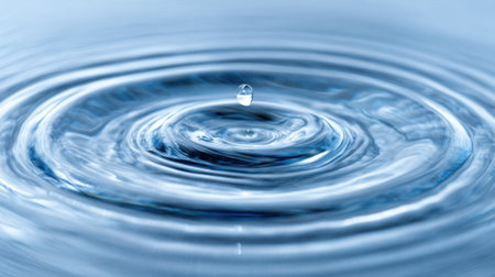 A drop of water falls into a tranquil surface producing beautiful circular ripples as it splashes.の素材