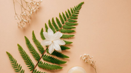 A serene display of green ferns and a white flower rests besides a small jar of natural skincare on a soft peach background, showing a calming and organic aesthetic.の素材