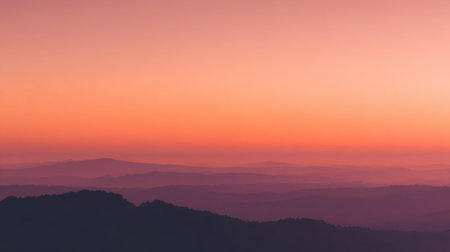 Vibrant hues of orange and purple blend softly above distant mountains at dusk.の素材