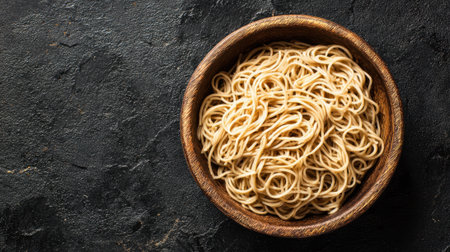 A bowl filled with perfectly cooked spaghetti sits on a dark textured surface. The noodles are presented simply, inviting tasty sauces and toppings to enhance the dish.の素材