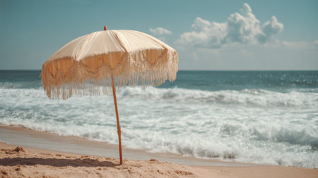 A vintage umbrella stands on a sandy beach providing shade as gentle ocean waves crash nearby. The bright blue sky enhances the peaceful atmosphere inviting relaxation and enjoyment.の素材