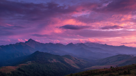 A breathtaking sunset fills the sky with vibrant colors above a remote mountain range. Soft clouds drift as shadows stretch across the peaceful valley below creating a serene atmosphere.の素材