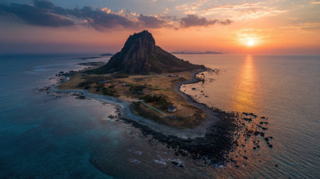 Golden light from the setting sun casts a warm glow on the tranquil island surrounded by ocean waves, highlighting the rugged cliffs and sandy patches. A peaceful scene unfolds in the evening sky.の素材