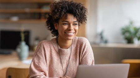 A cheerful young woman engages with her laptop in a warm and inviting room filled with natural light.の素材