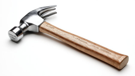 A heavy duty hammer rests on a white surface showing its shiny metal head and wooden handle ready for tasks.の素材