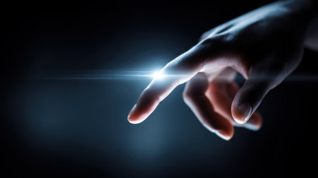 A hand reaches out gently touching a bright light in a dark environment sparking curiosity.の素材