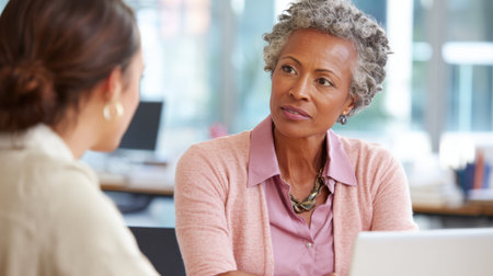 Two women share ideas and insights in a bright modern office fostering a collaborative atmosphere.の素材