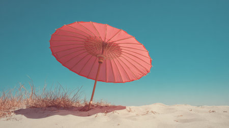 A vibrant pink umbrella is set in the sand casting a shadow on the beach. The bright sky and sandy terrain create a peaceful and inviting atmosphere for relaxation.の素材