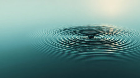 A smooth and reflective surface of water captures the soft hues of sunset while ripples expand after a drop creates a peaceful moment in nature.の素材