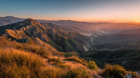 The sun sets behind the mountains casting golden light over the rolling hills and a peaceful valley. Lush greenery contrasts with rocky terrain in a serene natural setting.の素材