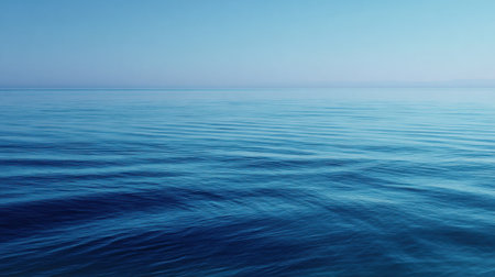 Gentle waves ripple across the serene ocean surface under a bright blue sky. The peaceful scene captures the beauty of nature at dawn by the coast.の素材