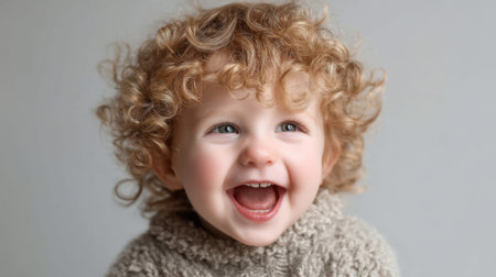 Happy caucasian child with curly hair laughing in cozy sweater.の素材