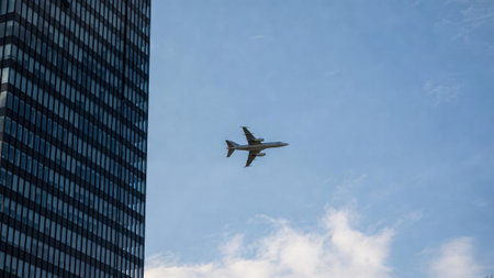 Airplane flying near skyscraper against blue sky and clouds.の素材