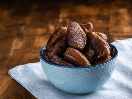 Dates of fruit in a blue ceramic bowl close up on wooden background. Horizontal. Copy space.