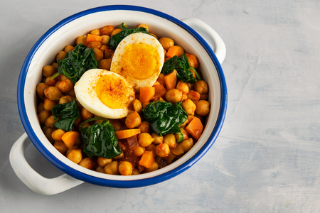Spanish chickpea and spinach stew with eggs on light gray background with copy space. Spanish cuisine. Traditional Spanish recipe prepared in Holly Week and Lent. Vegan Potaje de vigilia. Horizontal.の写真素材