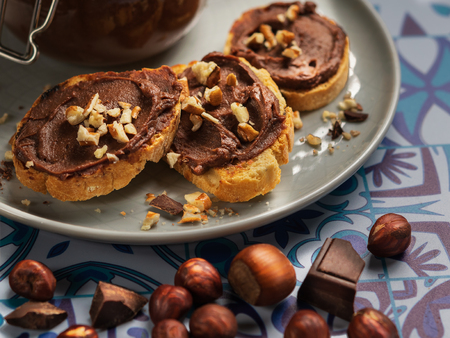 Homemade hazelnut cream in bowl with hazelnut nuts and slices of toast with chocolate cream on wooden background with copy space. Horizontal View. Still life.の写真素材